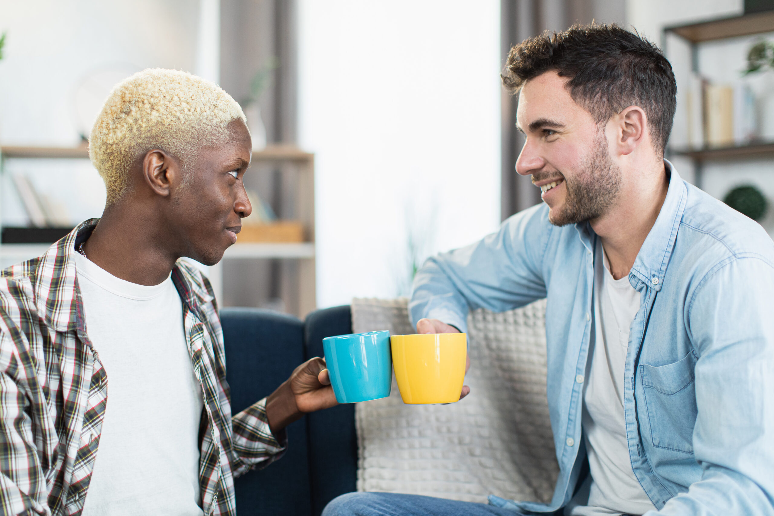 A content gay couple in New York City, enjoying quality time together in their cozy living room with cups of coffee, after successfully enhancing their sex life and relationship through sex and schema therapy at GayCouplesTherapy.com, which has helped them achieve greater intimacy and happiness in their day-to-day lives.